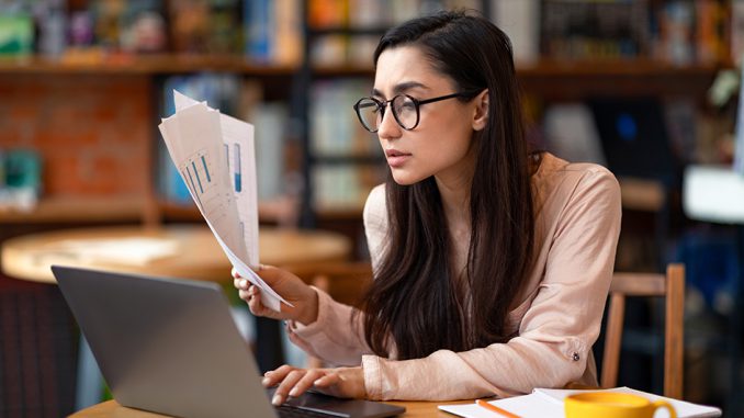 Successfull latin female entrepreneur working while sitting at cafe, using laptop and checking documents, copy space